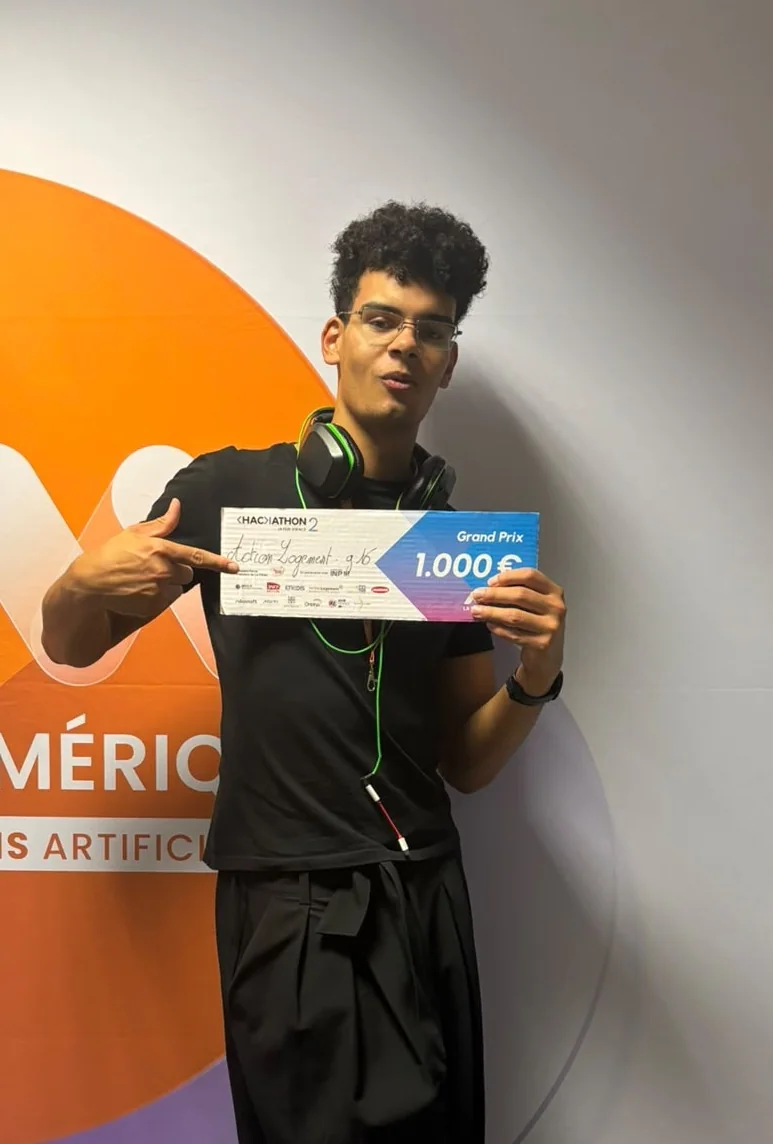 Alexis tient le chèque du grand prix du hackathon, 1 000 €, devant le mur de l’événement